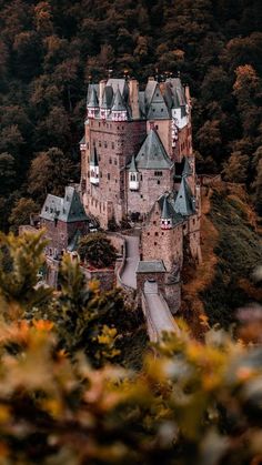 an aerial view of a castle in the middle of trees and hills with fall foliage around it