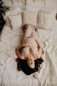 a woman laying on top of a bed in a room with white walls and pillows