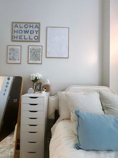 a white bed sitting next to a dresser with pictures on the wall above it in a bedroom