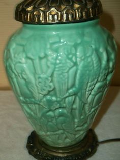 a green vase sitting on top of a table next to a light fixture with a gold lid