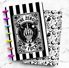 two black and white notebooks with colorful markers on the pages, one has a hand drawn