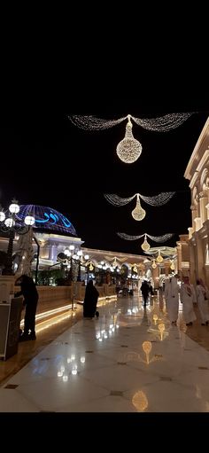 people are walking down the street at night with lights strung overhead and decorations hanging from the ceiling