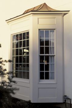 a white building with two windows and a small pine tree in front of the window