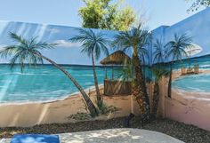 a mural on the side of a building with palm trees and a hut in the background