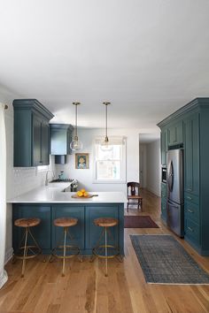 a kitchen with blue cabinets and wooden floors, two stools in the middle of the room