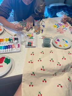 a woman sitting at a table with paint and watercolors on the table next to her