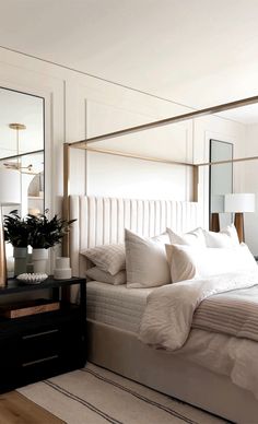 a bed with white sheets and pillows in a bedroom next to a mirror on the wall