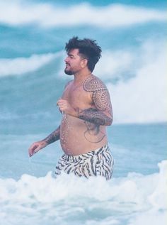 a man with tattoos on his body walking in the ocean