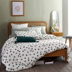 a bed with green and white polka dot bedspread in a small room next to a table