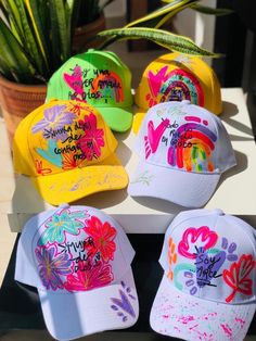 four hats with different designs on them sitting on a table next to a potted plant