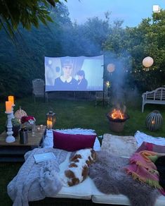 an outdoor movie is set up in the backyard with pillows and blankets on it, next to a fire pit