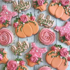 decorated cookies with pink and orange frosting are arranged on a wooden surface, including one that says baby