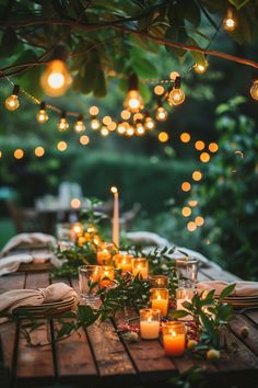 an outdoor dinner table with candles and greenery on the table, surrounded by hanging lights