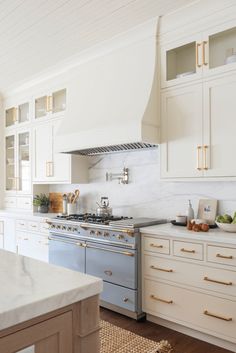 a kitchen with white cabinets and gold pulls on the stove top, along with an island