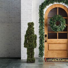 a wooden door with a wreath on it next to a tall green plant and a fake man