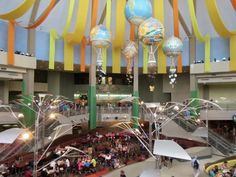 an indoor mall filled with lots of people and umbrellas hanging from the ceiling above