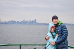 a man and woman standing next to each other on a boat near the water with a city in the background