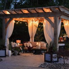 an outdoor living area is lit up with string lights and draping over the couches