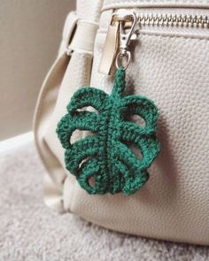 a green crocheted leaf is attached to a white purse