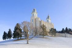 a large white building with two towers and trees in front of it on a snowy hill