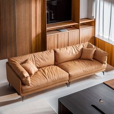 a tan leather couch sitting in front of a wooden entertainment center with a flat screen tv mounted on it's wall