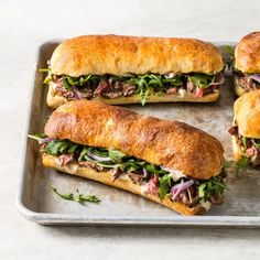 four sub sandwiches sitting on top of a metal tray with lettuce and meat