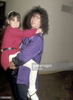 a woman holding a child in her arms while standing next to a man with curly hair