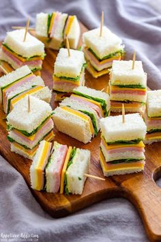 small sandwiches are arranged on a cutting board with toothpicks stuck in the middle