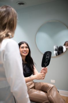 a woman sitting in front of a mirror holding a hair dryer