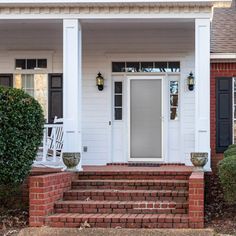 the front porch of a white house with black shutters and two chairs on it