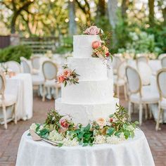 a white wedding cake sitting on top of a table covered in flowers and greenery