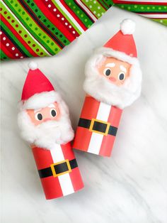 two toilet paper roll santas sitting on top of a white marble counter next to christmas decorations