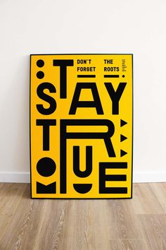 a yellow poster that says stay true on the floor next to a white wall and wooden floors