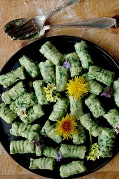 a black plate topped with dumplings covered in green sauce and flowers next to a fork