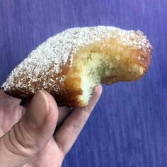 a hand holding a powdered donut with one bite taken out of the doughnut