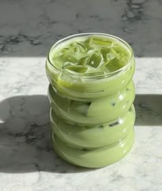 a glass filled with green liquid sitting on top of a marble counter next to a white wall