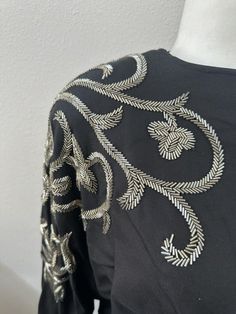 Elevate your formal look with this stunning Bonnie Boerer blouse from the 80s. The black silk blend blouse features batwing sleeves with intricate beading details. This blouse is a size M, with long sleeves and shoulder pads for added structure. The material is a combination of silk and cotton, making it both elegant and comfortable. The blouse is pre-owned and in great condition. Add this formal blouse to your wardrobe and make a statement at your next event. Clear acrylic rhinestones buttons at back of neck and on sleeve hems All bugle beads appear to be in place. Pit to pit 22 Length 25 Embroidered Long Sleeve Blouse For Evening, Elegant Embroidered Evening Tops, Long Sleeve Embroidered Blouse For Evening, Silk Embroidered Evening Tops, Elegant Embroidered Tops For Evening, Elegant Long Sleeve Embellished Tops, Evening Silk Blouse With Pearl Embroidery, Formal Black Embellished Blouse, Elegant Embroidered Tops For Night Out