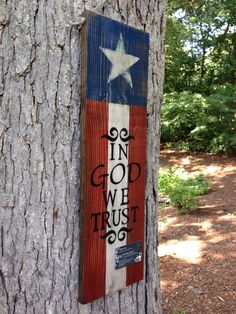 a wooden sign that says, in god we trust the texas flag on a tree