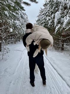 a man carrying a baby in the snow with trees behind him and one dog on his back