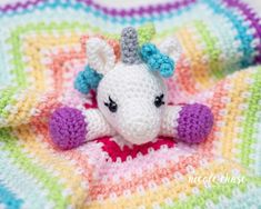 a small crocheted stuffed animal laying on top of a colorful blanket in the shape of a unicorn