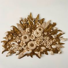 a decorative wall hanging made out of gold leaves and flowers on a white wall in a room