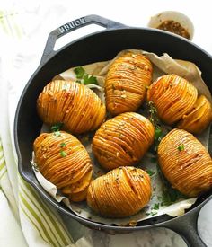 baked potatoes in a skillet on a marble counter top next to a spoon and napkin