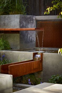 an outdoor fountain with water running from it's sides and plants growing on either side