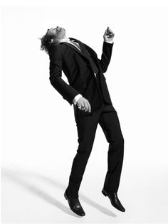 a man in a tuxedo is posing for a black and white photo with his hands in the air