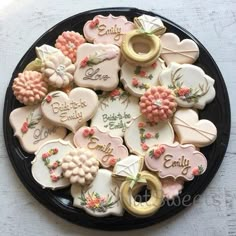 a black plate topped with cookies covered in frosting and decorated like flowers, hearts, and words