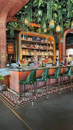 a bar with green chairs and plants hanging from it's ceiling above the bar