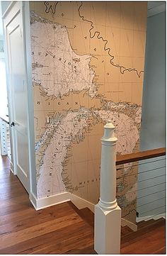 a wall with a map on it next to a banister in a room that has wood floors