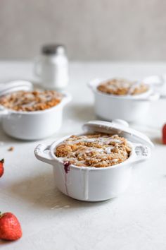 three small white dishes filled with food on top of a table next to strawberries