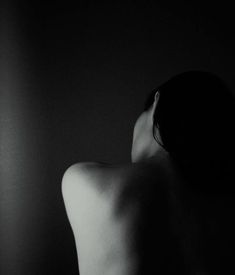 black and white image of a naked woman in the dark with her head tilted back