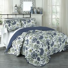 a bed with blue and white flowers on the comforter in front of a fireplace